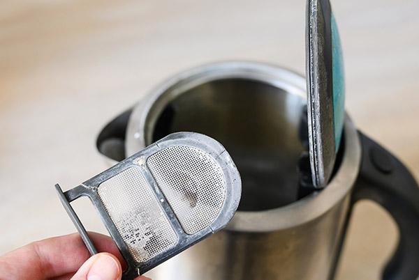 a person holding a metal mesh strainer over a kettle