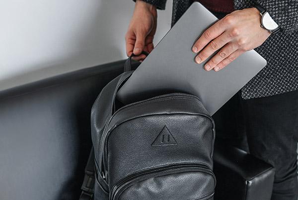 a man holding a laptop in his backpack while sitting on a couch