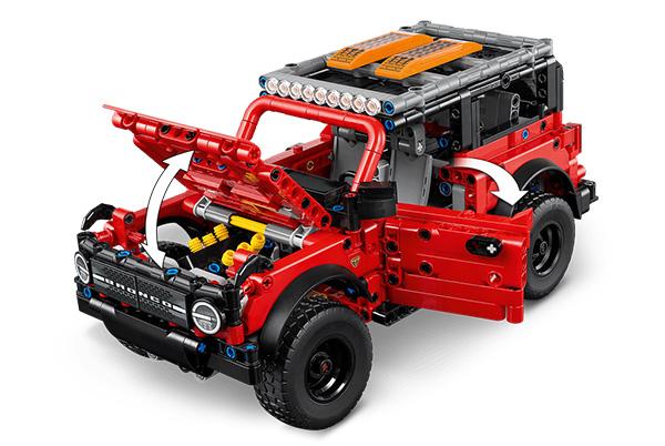 a red lego vehicle with a hood open and a box on the ground