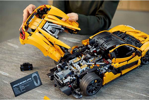 a person is holding a yellow lego car with a broken wing