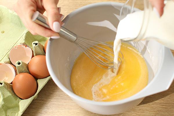 a person mixing eggs and milk in a bowl with a whisk