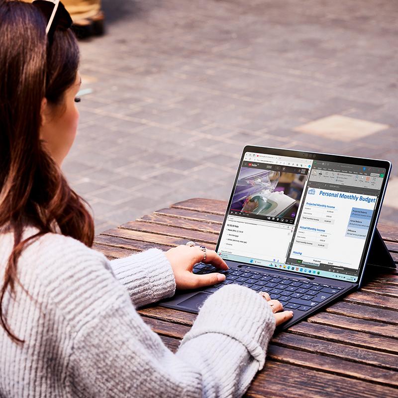 A woman sitting at a table multi-tasking on a Surface Pro