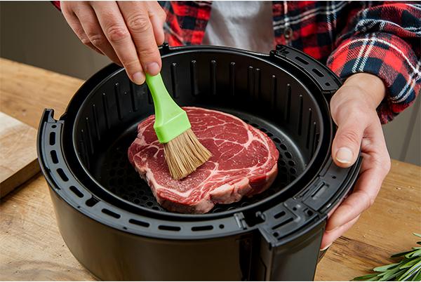 a person using a brush to clean a steak in an air fryer