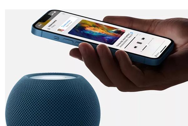 a person holding a smart phone next to a siri speaker