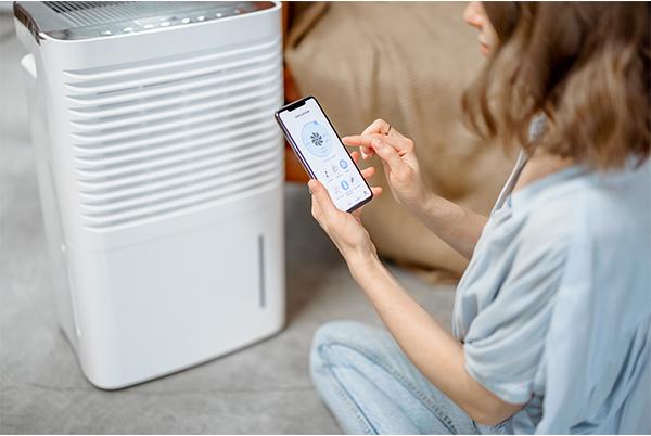 a woman sitting on the floor with a smart phone in front of a white air purifier