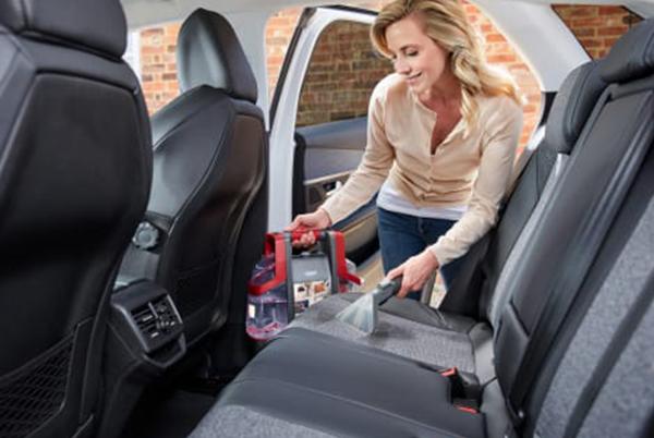 a woman in a car cleaning the seats with a Vax Spotwash vacuum