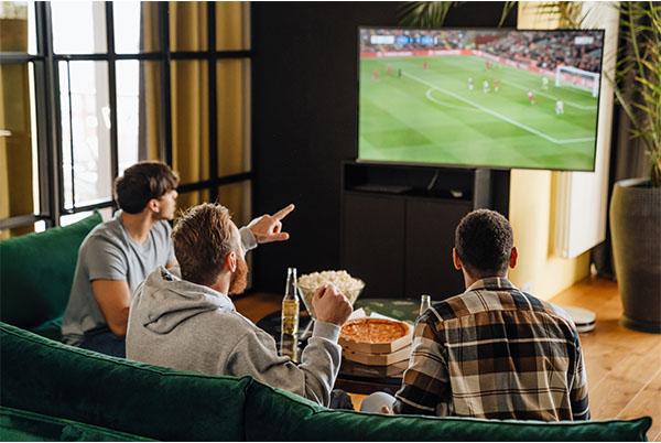 three men sitting on a couch watching a soccer game on a television