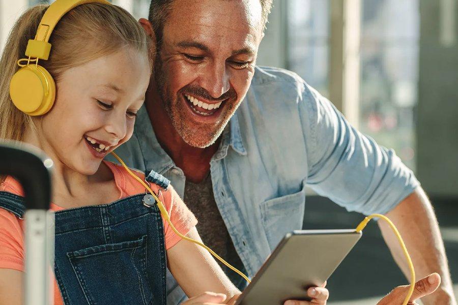 A man and cild look at a tablet whilst smiling
