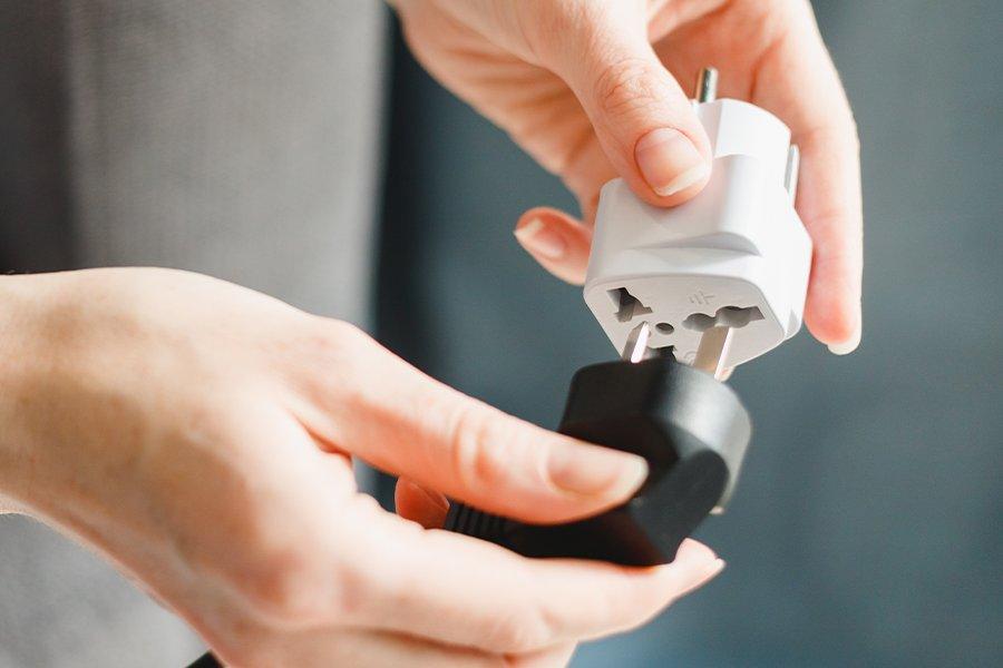 A pair of hands putting a plug into a travel adaptor