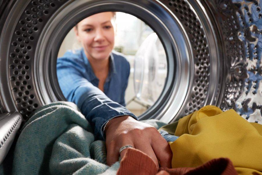 A woman reaching into the drum of a washing machine full of clothes