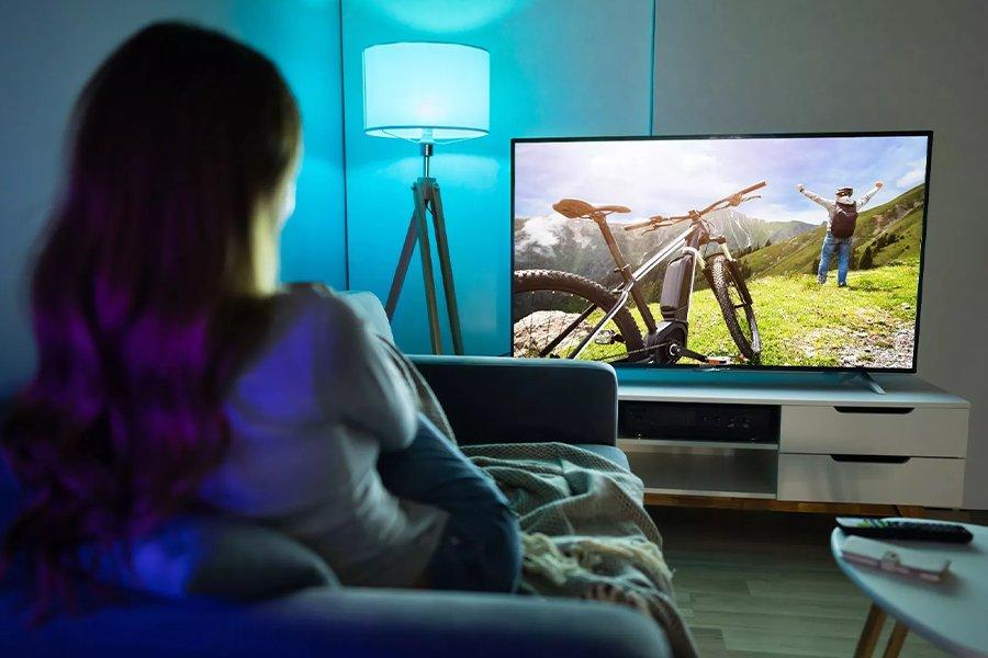 A woman watching a TV with a bike and a cyclist on it