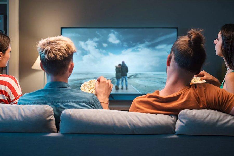 Four people sitting on a sofa watching a large TV