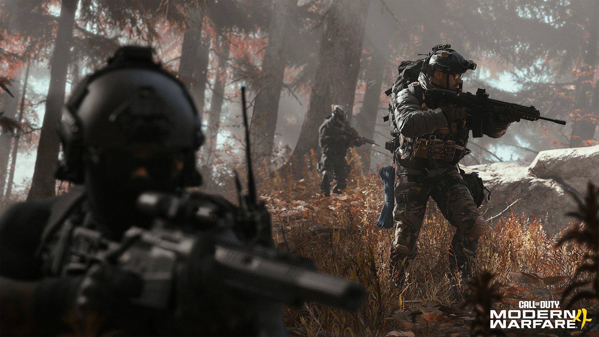 Three soldiers are walking through a forest whilst aiming their guns forwards