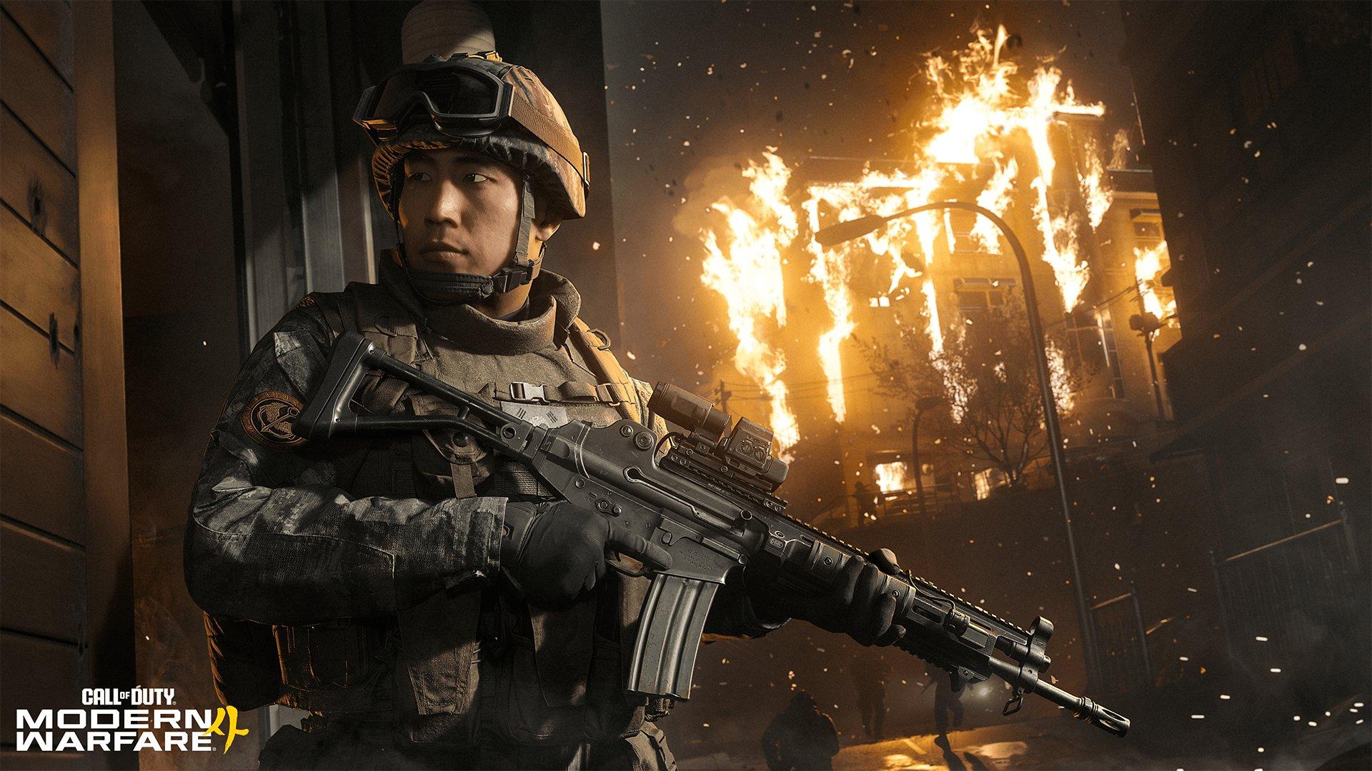 A soldier holding a fun stands in front of a burning building