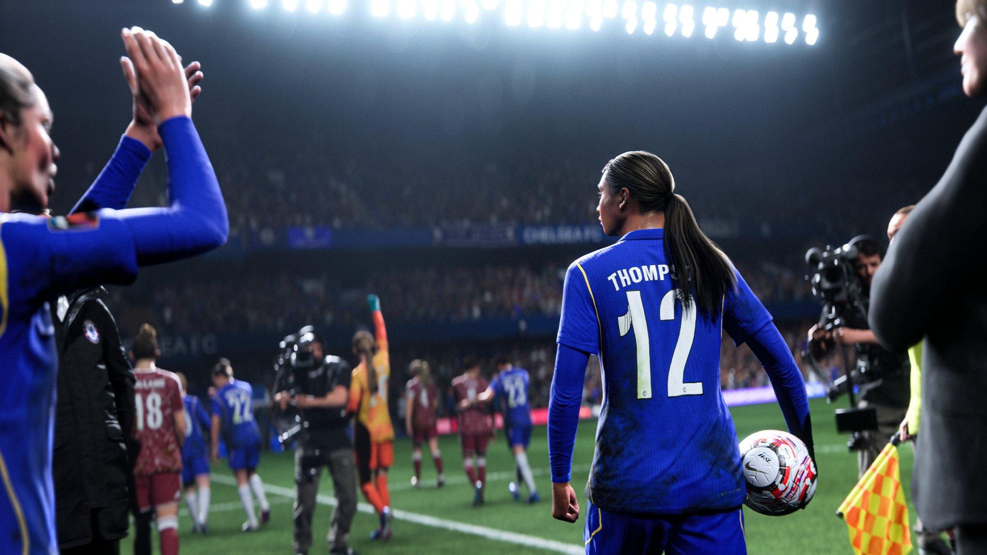 A football player in a blue kit is walking into a stadium whilst carrying a ball