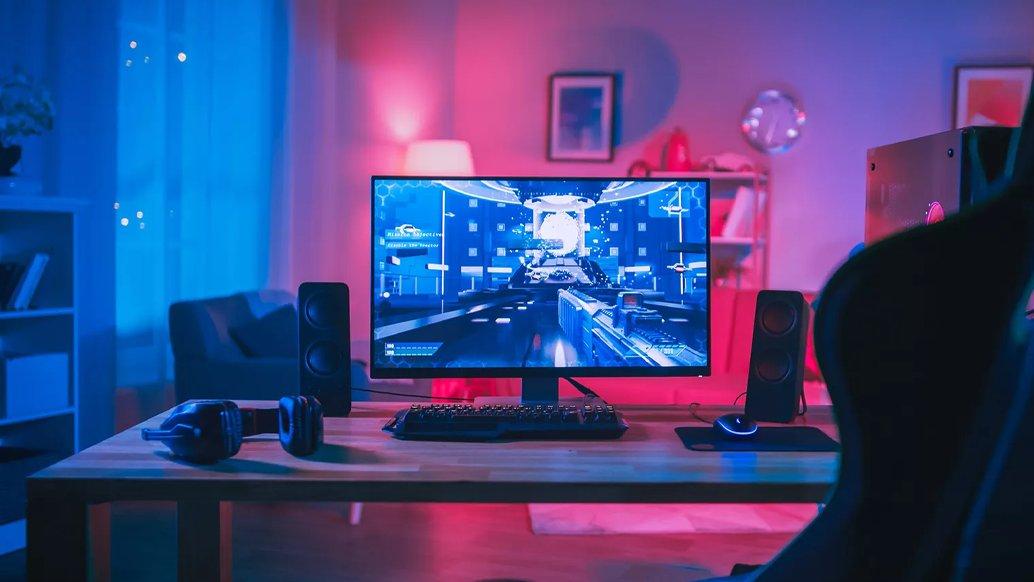 A computer set up on a desk with a pink, purple and blue glow behind it. 