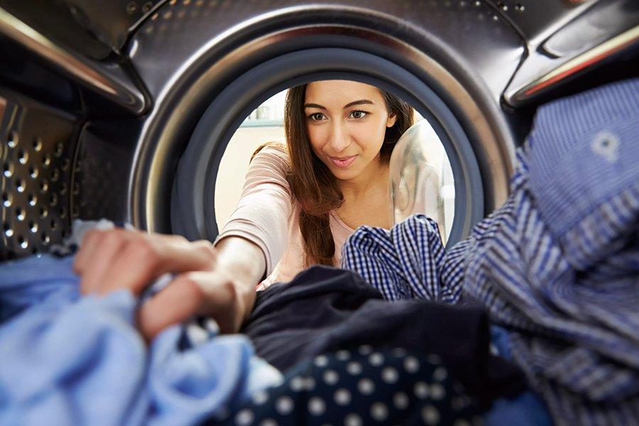 A woman reaching into a washing machine drum that has clothes in it
