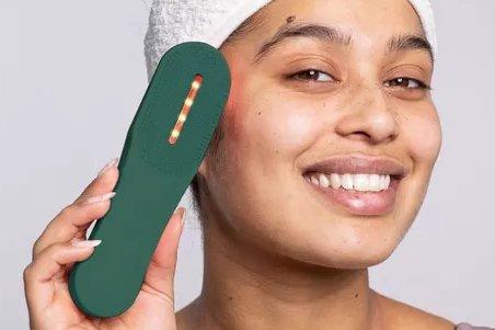 a woman with a towel on her head holding a green light therapy device