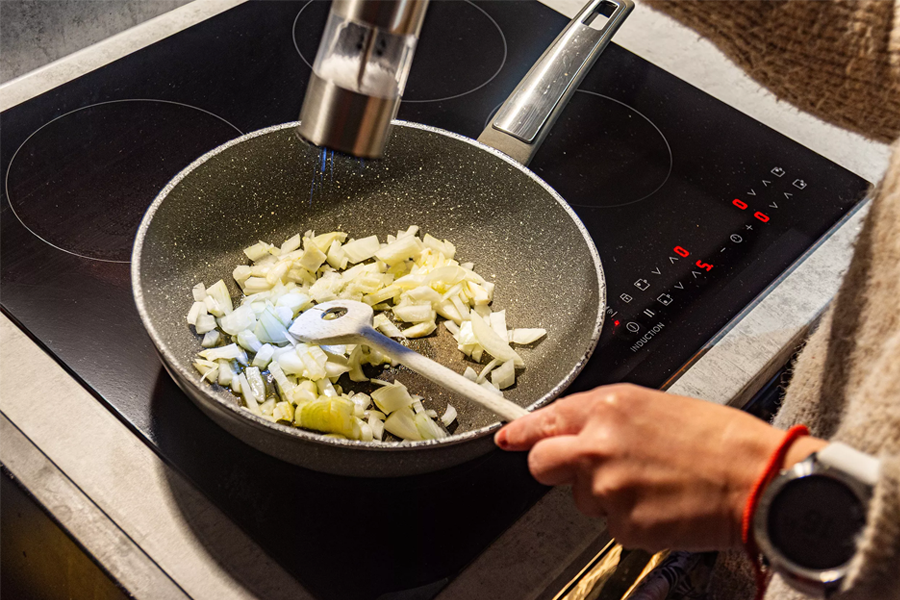 Chopped onions and potatoes being sautéed in a dark speckled pan on a induction hob
