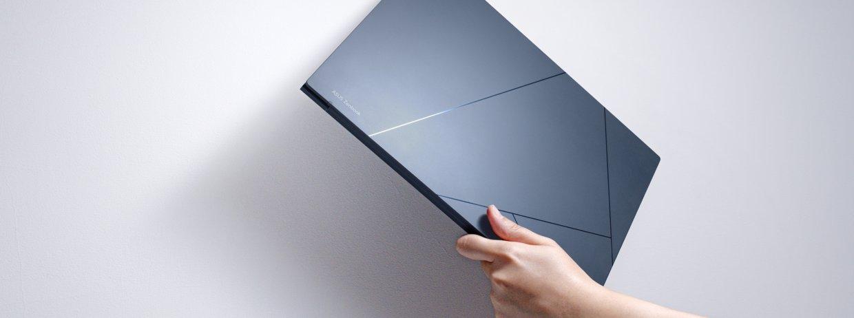 A hand holds up an ASUS laptop against a grey background